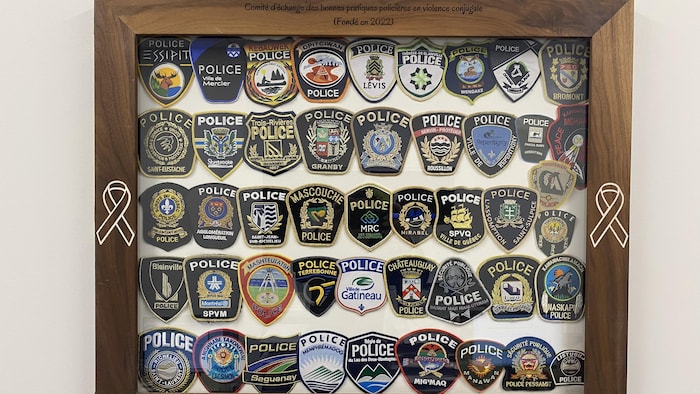 Une cinquantaine d'écussons représentant différents corps de police du Québec sont affichés dans un cadre en bois.