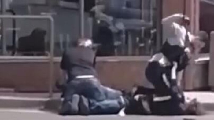Un agent de la GRC lève le poing au-dessus de la tête d'un homme plaqué au sol lors d'une arrestation. À côté d'eux, un autre homme est accroupi au-dessus d'un autre individu.