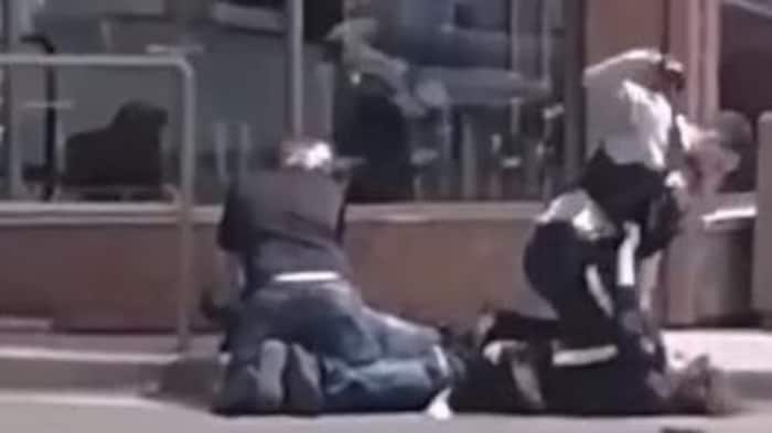 Un agent de la GRC lève le poing au-dessus de la tête d'un homme plaqué au sol lors d'une arrestation. À côté d'eux, un autre homme est accroupi au-dessus d'un autre individu.