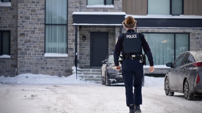 Un policier marche de dos devant une maison.