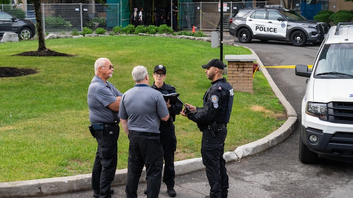 Quatre membres du corps de police, dont deux en uniforme, discutent à l'extérieur de la tour d'habitation.