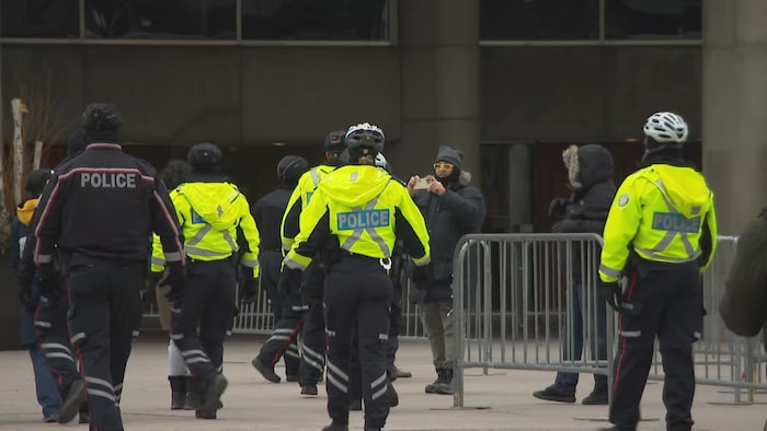 Six policiers qui s'avancent lors d'une manifestation pendant qu'un homme prend une photo.