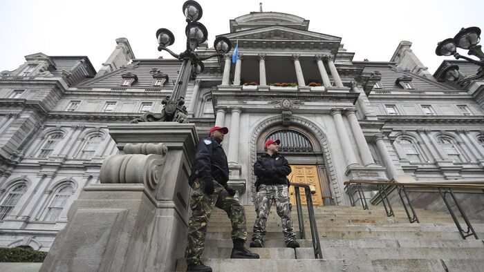 Deux policiers portant des pantalons de camouflage sont debout dans l'escalier devant l'hôtel de ville de Montréal.