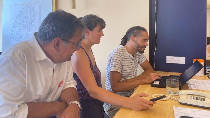 Deux hommes et une femme discutent sur une table de travail, regardant un écran d'ordinateur. L'un des hommes (à gauche) est Andrés Fontecilla, candidat de Québec Solidaire dans Laurier-Dorion.