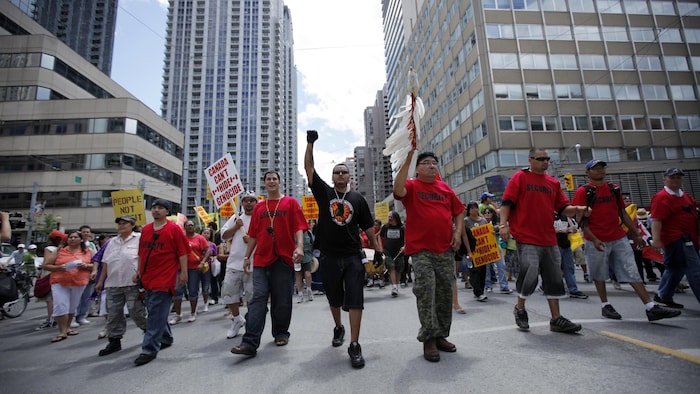 Des hommes marchent dans les rues de Toronto, vêtus de chandails rouge, et certains portent des pancartes.