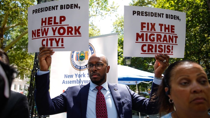 Un homme tient des pancartes sur lesquelles on peut lire : « Président Biden, aidez la ville de New York » et  « Réglez la crise des migrants ».