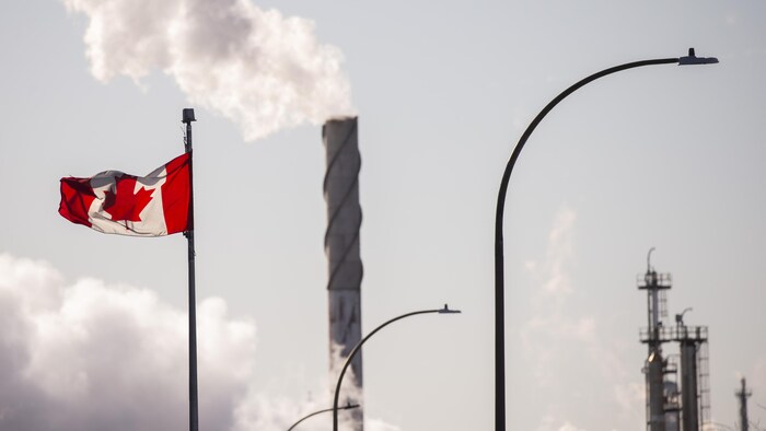 Un drapeau canadien avec, en arrière-plan, de la fumée qui sort d'une cheminée.