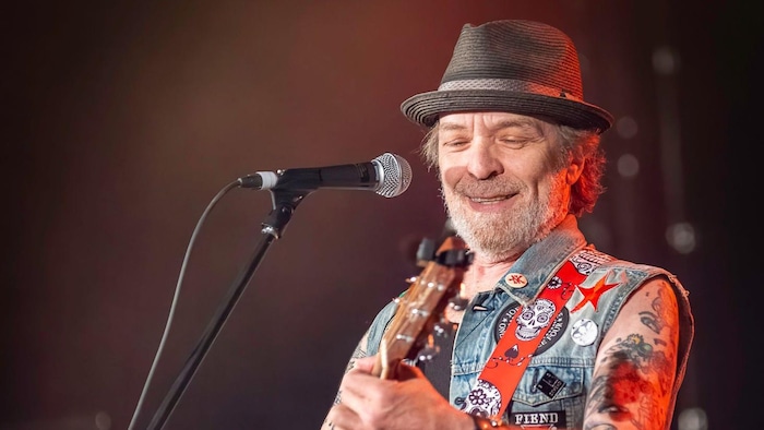 Un homme portant un chapeau joue de la guitare devant un micro.