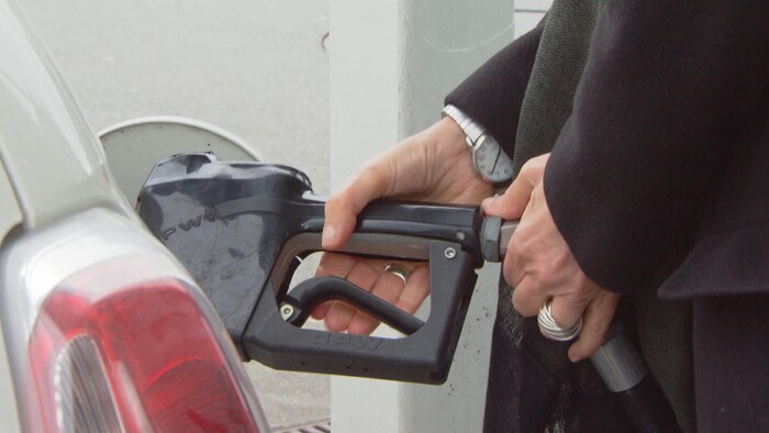 Une personne tient le pistolet d'une pompe à essence qui est inséré dans l'entrée du réservoir de sa voiture.