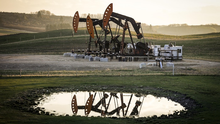 Des pompes extraient du pétrole et du gaz des têtes de puits alors que la fumée d'un incendie de forêt flotte dans l'air près de Calgary, en Alberta, le dimanche 12 mai 2024.