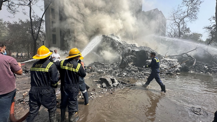 Des pompiers arrosent les décombres fumants.