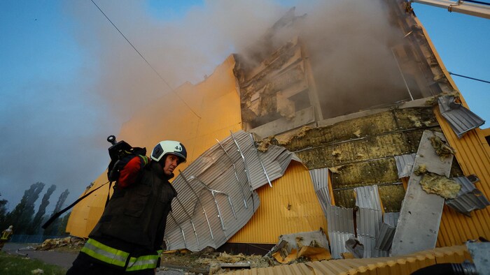 Un pompier devant les ruines d'un bâtiment en tôle éventré.