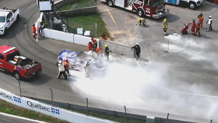 Des pompiers regroupés autour d'une voiture de course tentent de maîtriser les flammes à l'aide de leur équipement.