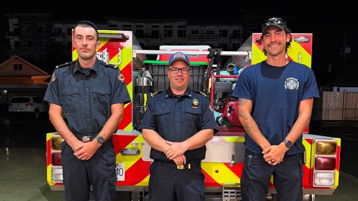 Des pompiers posent devant un camion de pompiers.