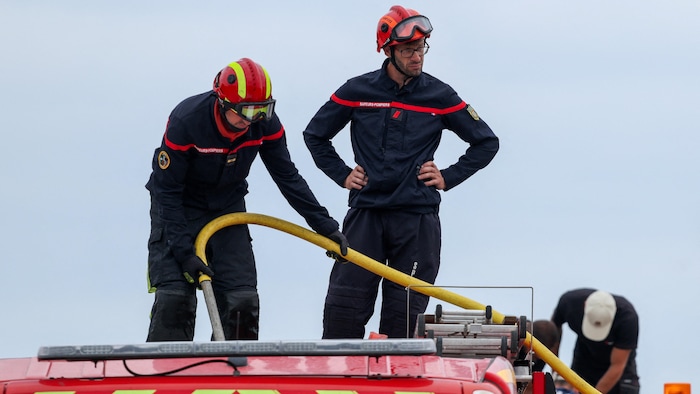 Deux pompiers sur le toit de leur camion.