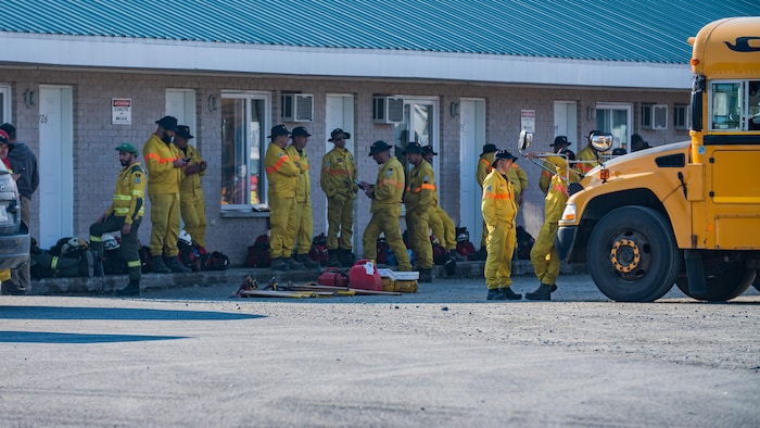 Des pompiers en uniforme devant un autobus scolaire.