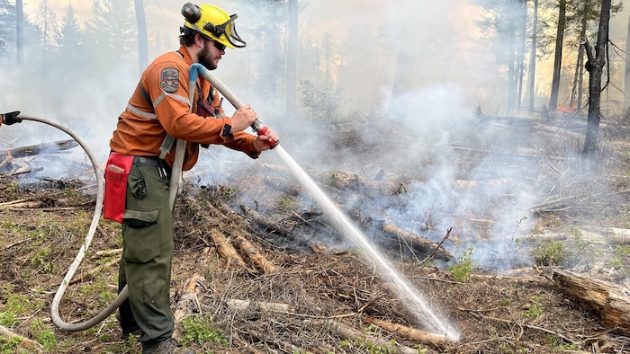 Un pompier forestier arrose avec un boyau pour éteindre un incendie de forêt.