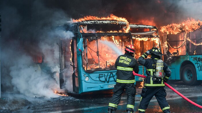 Deux pompiers arrosent des autobus enflammés.