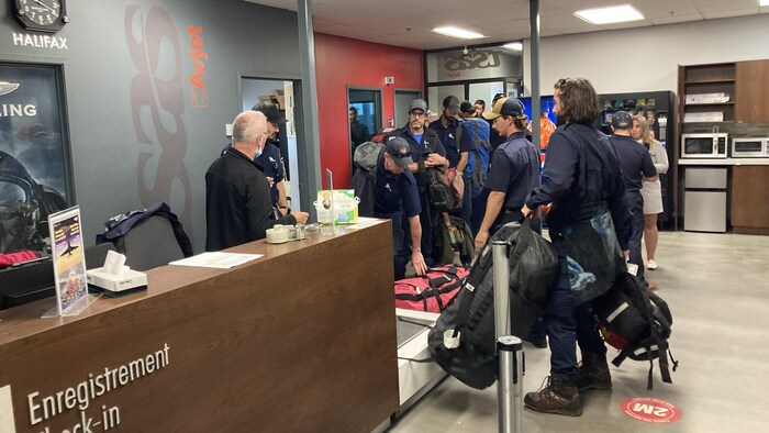 Des employés de la SOPFEU font la file devant un comptoir d’enregistrement à l’aéroport.