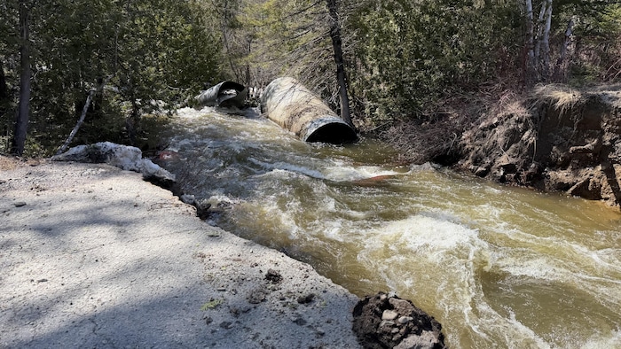 Un ruisseau agité traverse une route, des débris du ponceau se trouvent dans le lit du cours d'eau.