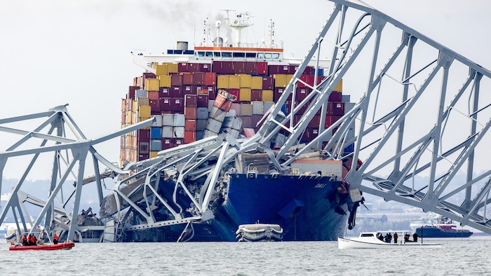 The container ship Dali is frozen in the water, under part of the bridge that collapsed after the ship collided. 