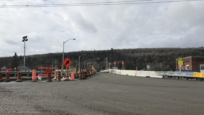 Route menant vers un pont en réfection avec de nombreux cônes et pancartes.