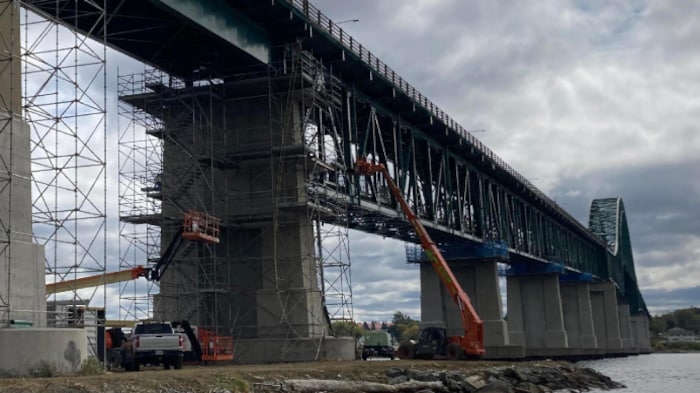 Des ouvriers sur des échafaudages effectuent des travaux sous le pont.