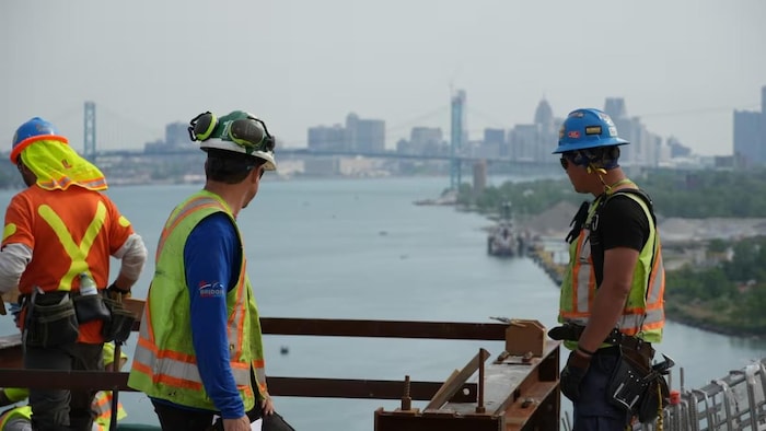 Deux travailleurs sont tournés vers le pont Ambassador, visible au loin.