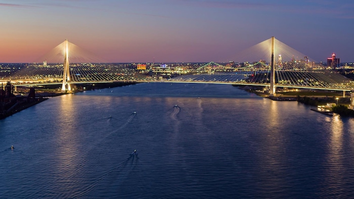 Le pont Gordie-Howe illuminé dans la pénombre avec la ville de Détroit derrière. 