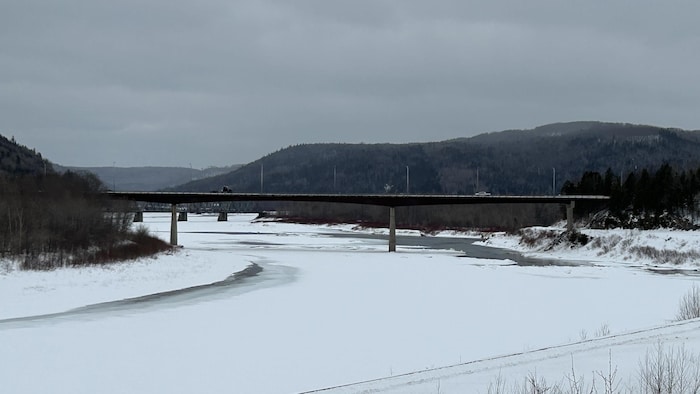 Un pont où deux véhicules circulent, au-dessus d'une rivière enneigée.