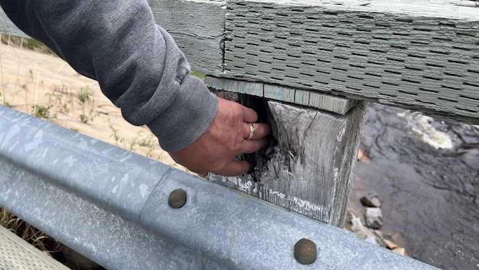 Une personne touche un morceau de bois pourri sur la garde d'un pont.
