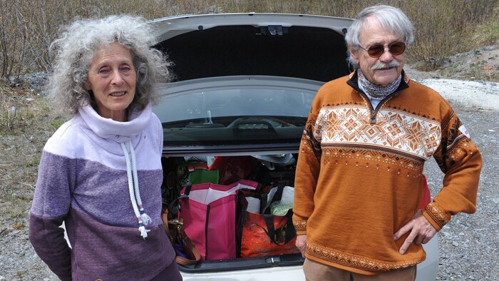 Deux personnes se tiennent devant le coffre arrière de leur voiture. Le coffre est ouvert et plein de sacs réutilisables.
