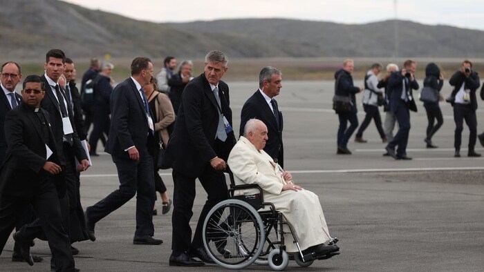 Pope Francis is being pushed in his wheelchair.