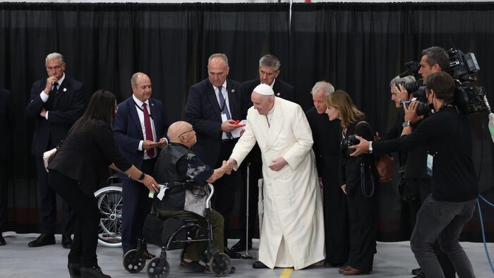 Le pape François serre la main d'un homme en fauteuil roulant.