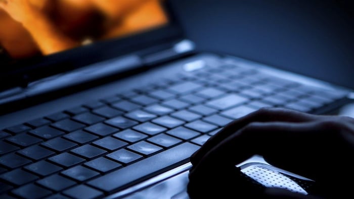 Une photo sombre montrant le clavier d'un ordinateur portable avec la main d'un homme posée dessus. On peut deviner que l'homme regarde de la pornographie sur l'écran.