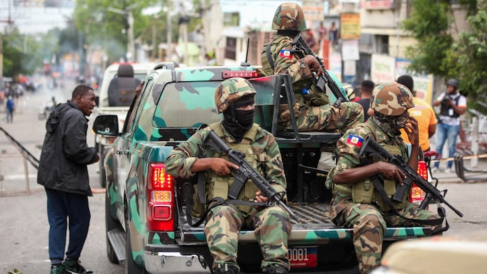 Trois membres de l'armée haïtienne assis à l'arrière d'une camionnette.