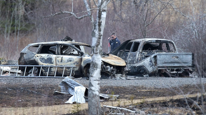 Un enquêteur entre deux véhicules complètement incendiés.