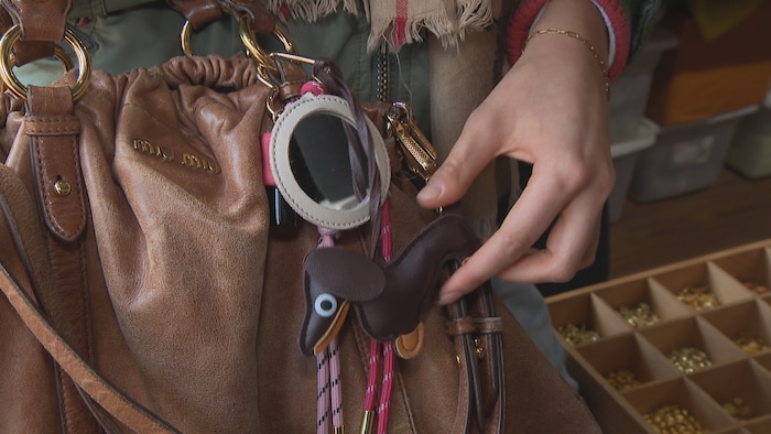 Un sac sur lequel est accroché un porte-clés en forme de chien, un petit miroir et d'autres petits accessoires.