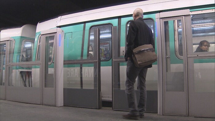 Des portes palières s'ouvrent dans une station de métro de Paris, en France, et un homme s'apprête à entrer dans une rame.