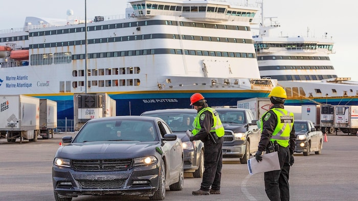 Des agents vêtus de vestes jaunes s'approchent des automobiles qui sortent du traversier amarré au quai.
