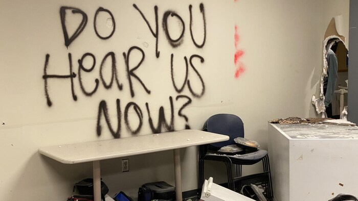 Une message en anglais écrit sur un mur à l'intérieur d'un commissariat de police saccagée dit : « Et maintenant, vous nous entendez? »