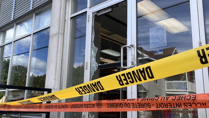 Une porte de verre fracassée avec des rubans de police.