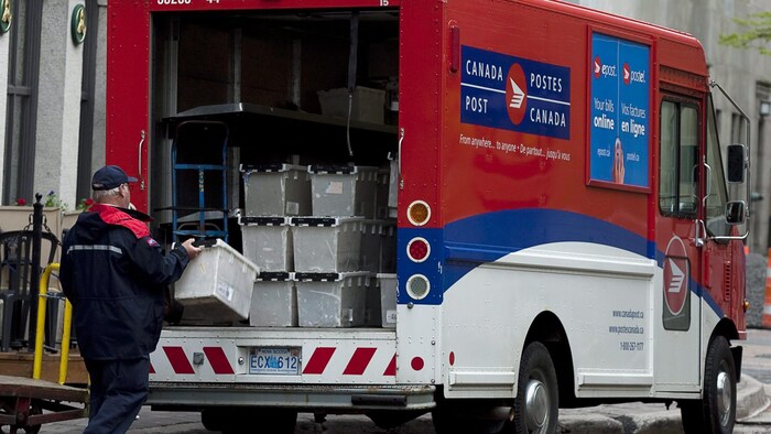 Un travailleur de Postes Canada sort une boîte de courrier d'un camion de livraison.