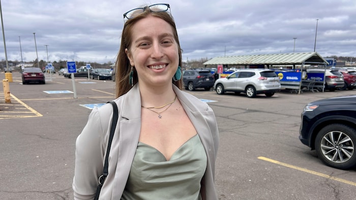 Une femme sourit à la caméra dans un stationnement.