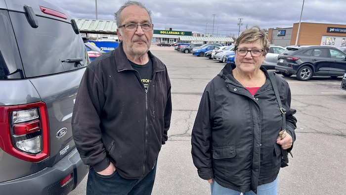 Deux personnes sourient à la caméra dans un stationnement.