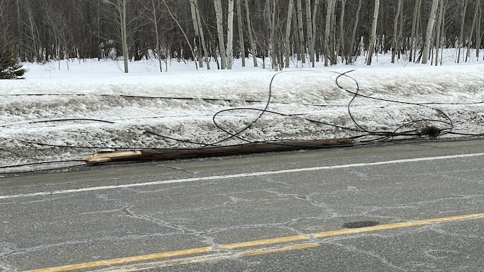 Un poteau de bois brisé et des fils sur les bord d'une route.