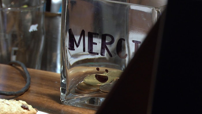 Un contenant de verre sur lequel il est écrit «merci» contient des pièces de monnaie.