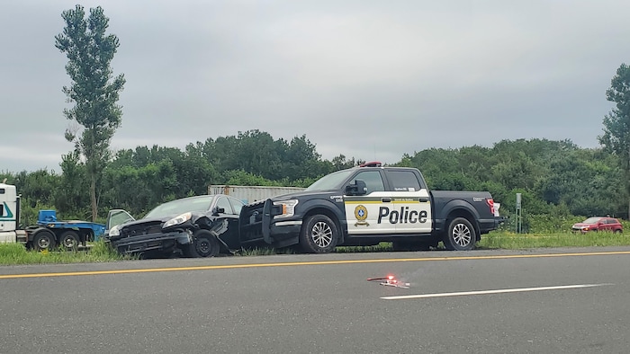 Le véhicule du suspect est endommagé sur le bord de l'autoroute à côté d'une camionnette de police.