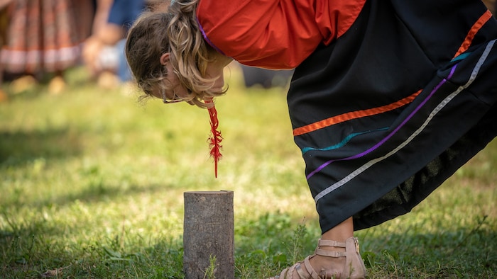 Une jeune fille se penche pour prendre une plume entre ses dents.