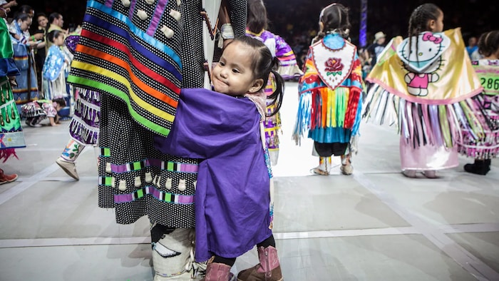 Une petite fille en costume traditionnel s'agrippe à la jambe d'un adulte lors du pow-wow de l'assemblée des nations à Albuquerque, au Nouveau-Mexique.